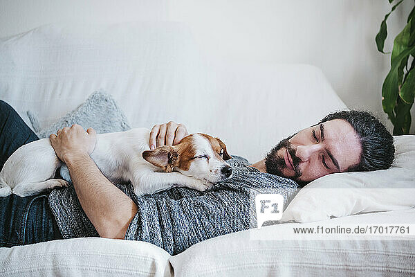 Man napping with dog while lying on sofa at home