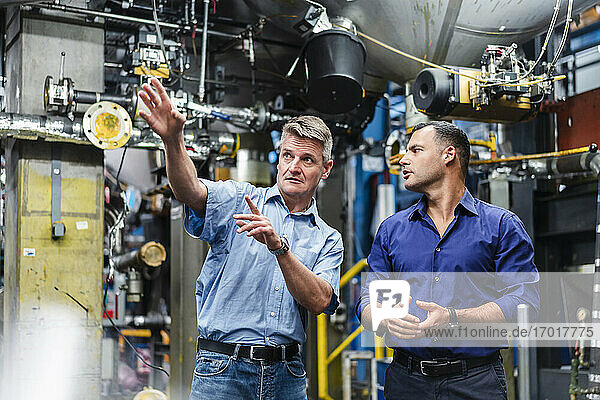 Mature male entrepreneur explaining to colleague while working in factory