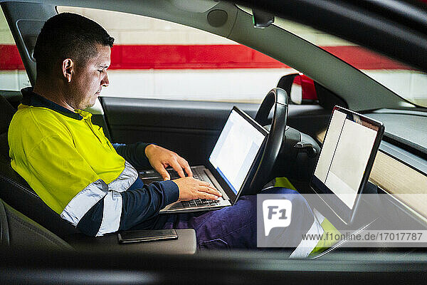 Männlicher Techniker programmiert am Laptop  während er in einem Elektroauto sitzt