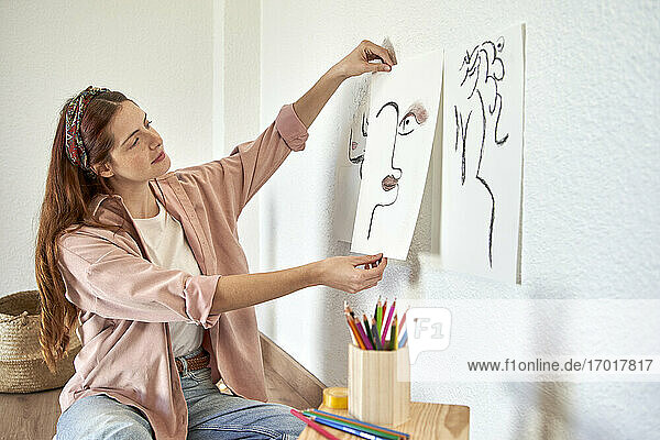 Weibliche Künstlerin  die eine Kohlezeichnung an die Wand im Wohnzimmer klebt
