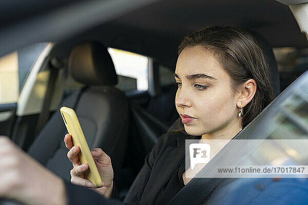 Geschäftsfrau  die im Auto sitzend ein Mobiltelefon benutzt