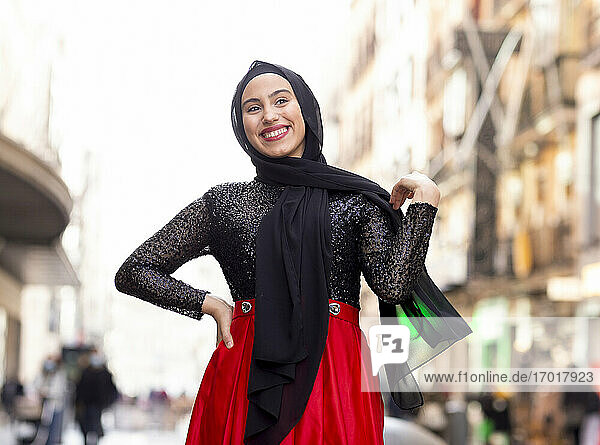 Porträt einer jungen Frau mit schwarzem Hidschab  die im Freien mit der Hand auf der Hüfte posiert
