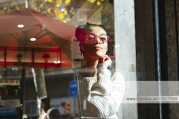 Confident young woman wearing eyeglasses looking through window at cafe
