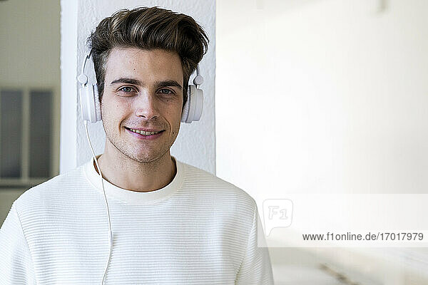Lächelnder junger Mann hört Musik über Kopfhörer an einer Säule in seinem neuen Haus