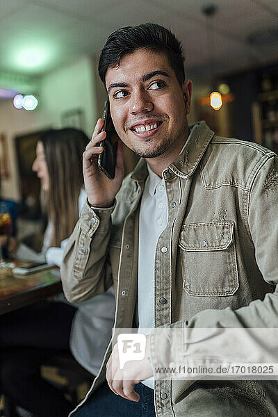 Lächelnder Mann  der in einer Bar mit dem Handy telefoniert und dabei wegschaut