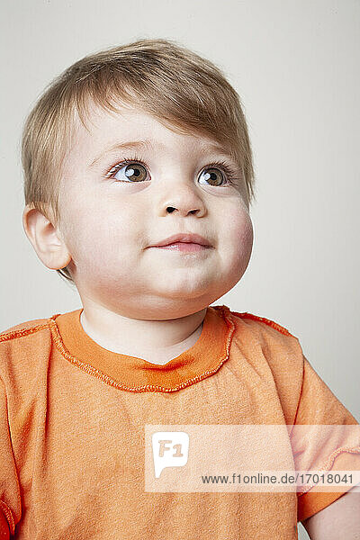 Kleiner Junge in orangefarbenem T-Shirt schaut nach oben