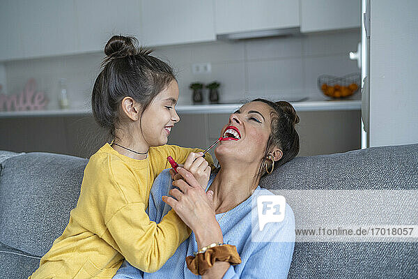 Lächelnde Tochter  die ihrer Mutter im heimischen Wohnzimmer Lippenstift aufträgt