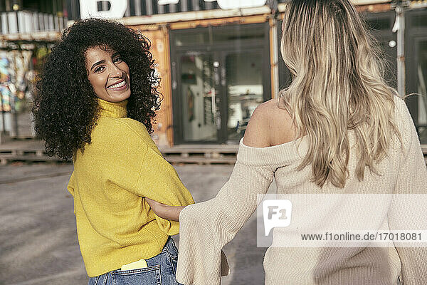 Lächelnde junge Frau steht mit einer Freundin auf einer Straße in der Stadt