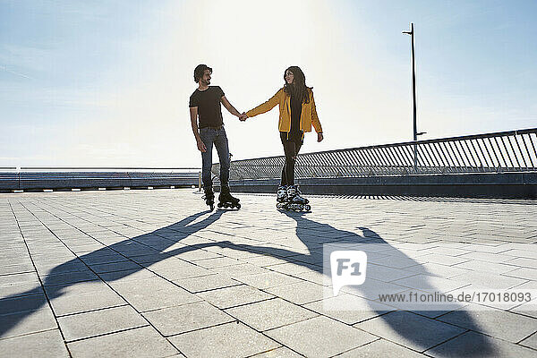 Junges Paar  das sich beim Rollschuhlaufen auf dem Pier an einem sonnigen Tag ansieht