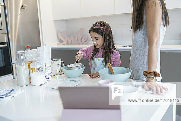 Tochter bereitet Muffin zu  während die Mutter in der Küche steht