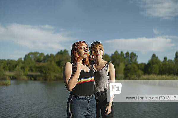 Young lesbian couple standing together by lake against sky