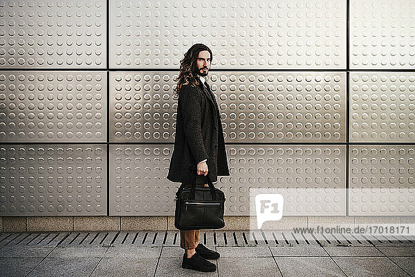 Businessman carrying briefcase while standing against silver wall