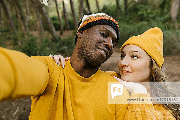 Mann mit Strickmütze  der ein Selfie mit einer Frau macht  während er im Wald steht
