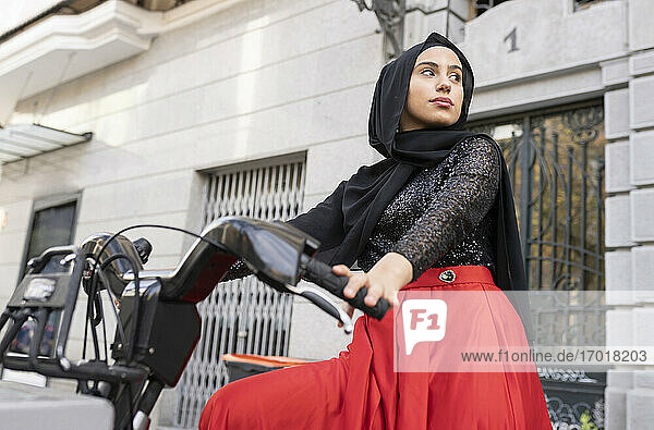 Portrait of young woman wearing hijab sitting on rental bike