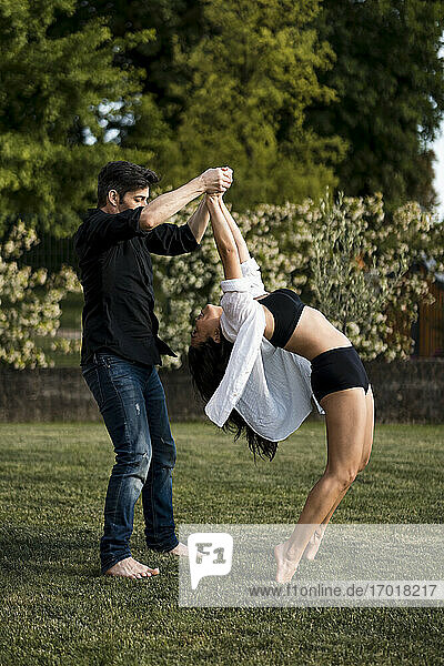 Male dancer holding hands of female dancer while standing on tiptoes and bending in back yard
