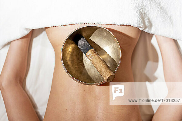 Mallet in rin gong on female customer's back lying on massage table at health spa
