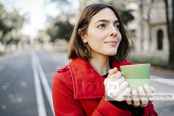 Junge Frau mit Kaffeetasse  die auf der Straße steht und träumt