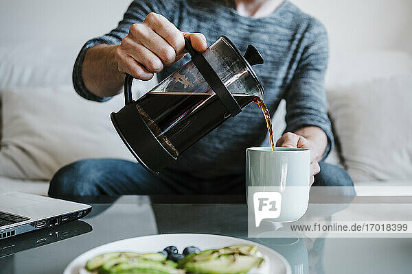 Man holding coffee maker while pouring coffee in coffee cup sitting at home