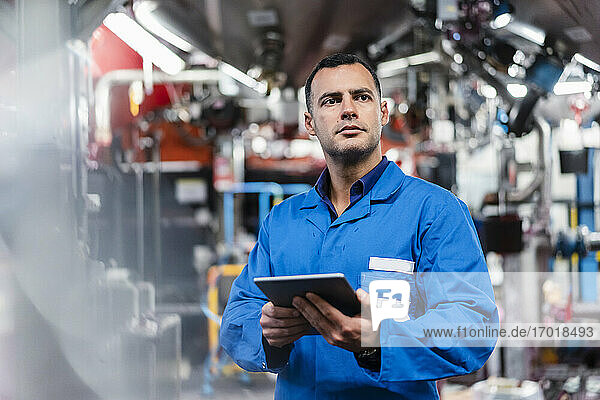 Confident male engineer holding digital tablet while looking away in factory