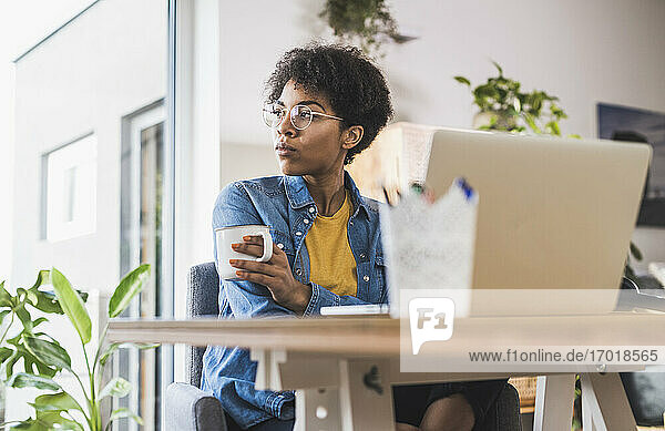 Frau hält Kaffeetasse  sitzt zu Hause vor dem Laptop