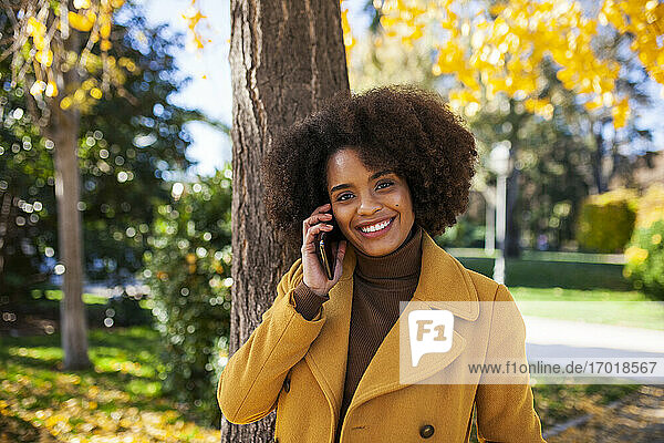 Smiling woman talking on mobile phone while standing at park