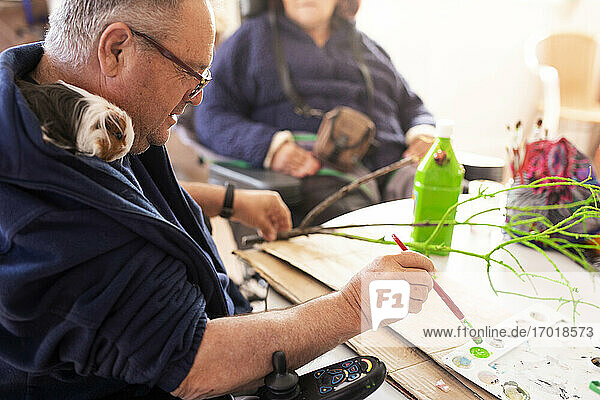 Älterer behinderter Mann malt einen Zweig im Rehabilitationszentrum