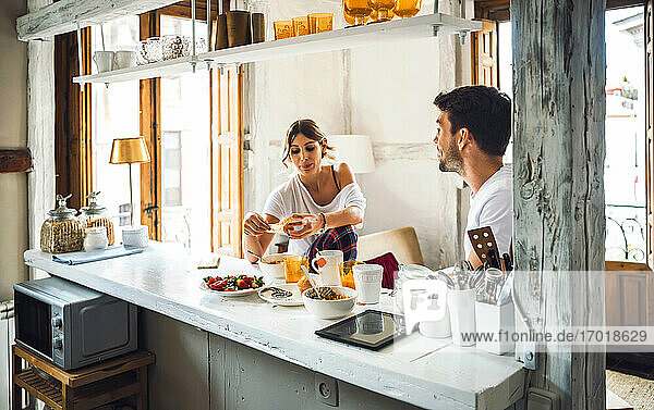 Young couple sitting at table and having breakfast at home