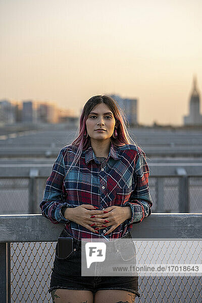 Hipster young woman leaning on railing during sunset