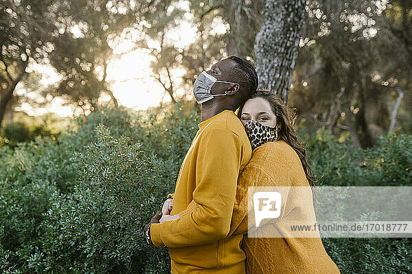 Frau mit Gesichtsschutzmaske umarmt Mann im Wald stehend