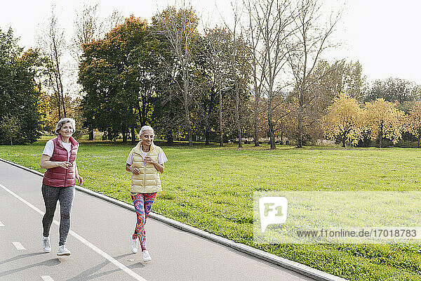 Lächelnde Freundinnen joggen im öffentlichen Park an einem sonnigen Tag