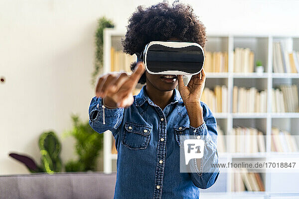 Frau mit Virtual-Reality-Headset  die ihre Hand ausstreckt  während sie zu Hause steht