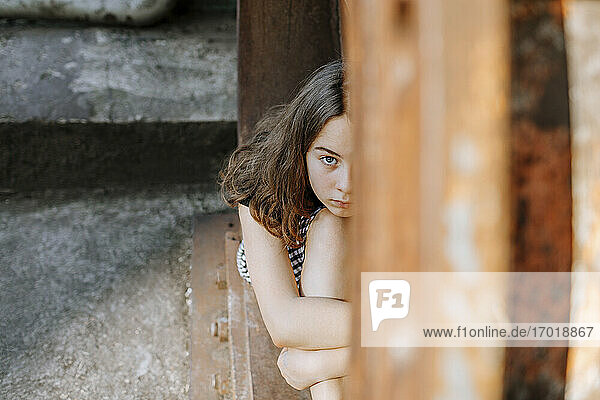 Teenage girl hugging knees while sitting on abandoned window sill