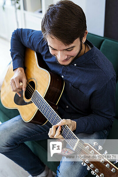 Gitarrist spielt Akustikgitarre  während er auf dem Sofa im Studio sitzt