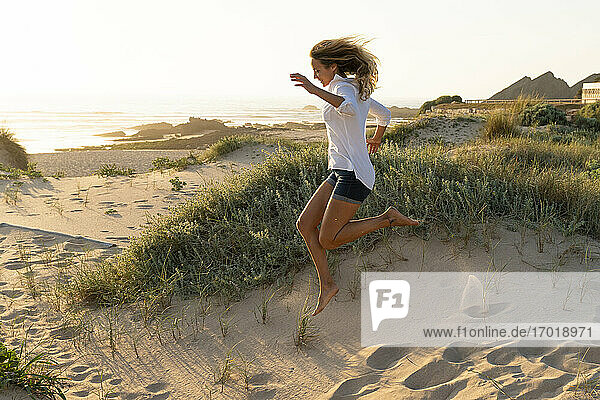 Carefree woman jumping on sand at beach during sunset