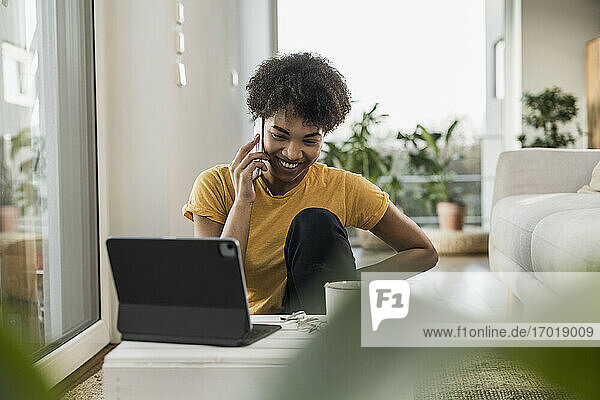 Lächelnde Frau mit digitalem Tablet  die zu Hause sitzt und mit ihrem Mobiltelefon spricht