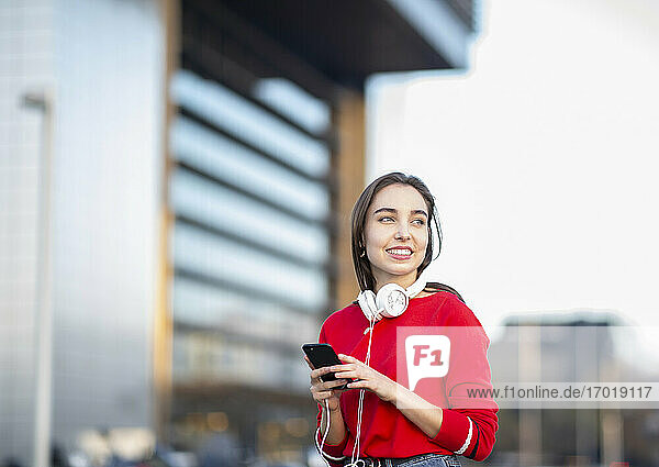 Lächelnde Frau mit Kopfhörern und Mobiltelefon in der Stadt