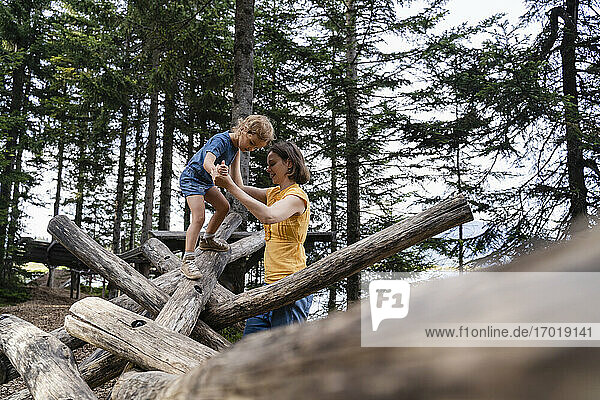 Mutter  die ihrer kleinen Tochter beim Gehen auf einem Holzstamm hilft