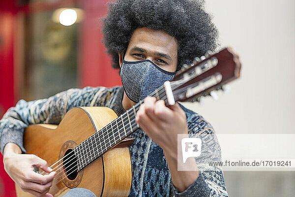 Young man wearing face mask playing guitar while sitting outdoors