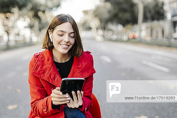 Lächelnde modische Frau  die ein digitales Tablet benutzt  während sie auf dem Sitz auf der Straße Musik hört