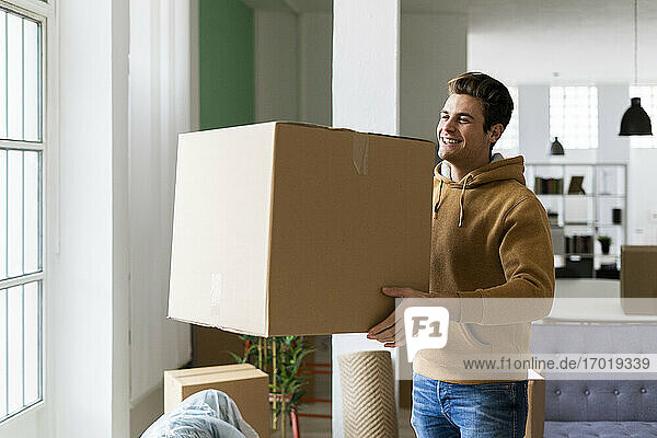 Glücklicher junger Mann mit Kiste in neuer Loftwohnung