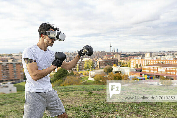 Männlicher Akrobat mit Virtual-Reality-Headset übt Boxen auf einem Hügel in der Stadt