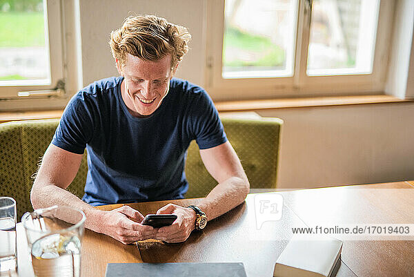 Lächelnder Mann  der sein Smartphone über einem Tisch zu Hause benutzt