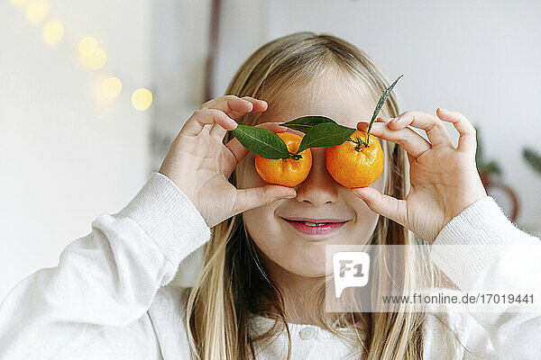 Nahaufnahme eines lächelnden Mädchens mit Mandarinen auf den Augen