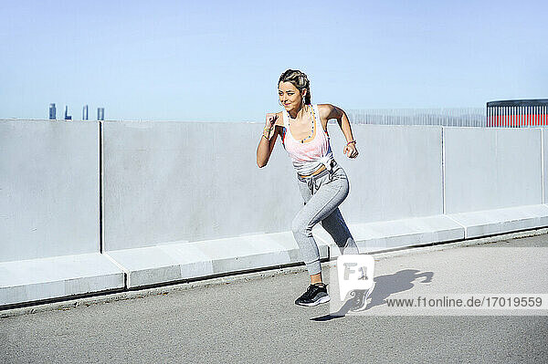 Young female athlete exercising while running on footpath during sunny day