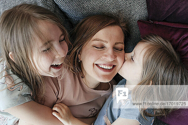 Happy daughters embracing mother while lying down on couch at home