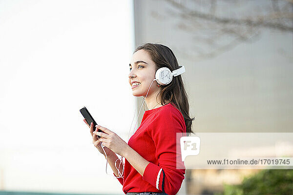 Glückliche Frau hört Musik über Kopfhörer  während sie ein Mobiltelefon hält