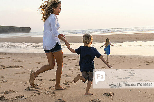 Cheerful mother running while playing with children at beach