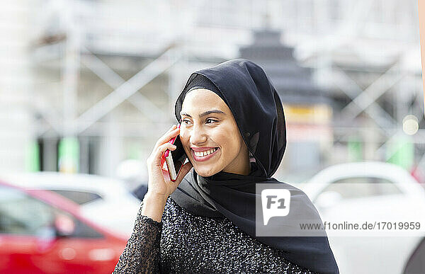 Porträt einer jungen schönen Frau mit schwarzem Hidschab  die mitten auf der Straße mit einem Smartphone telefoniert