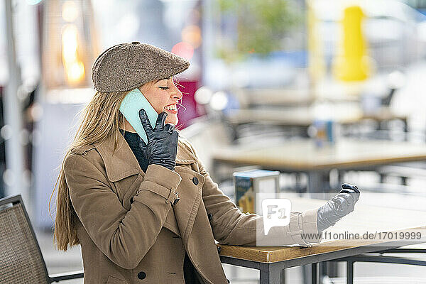 Smiling woman talking on smart phone at sidewalk cafe