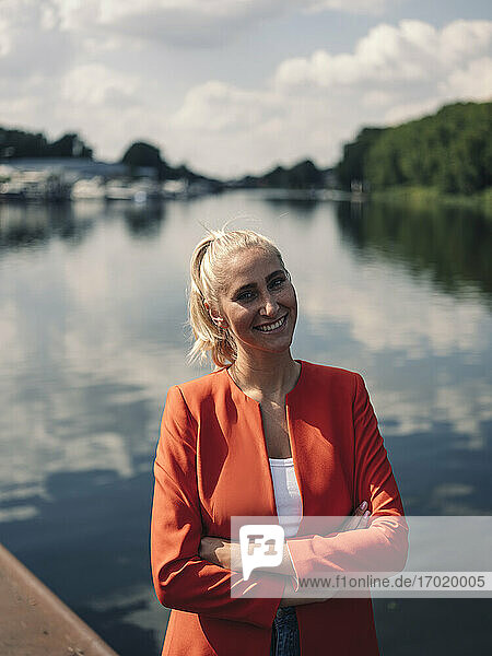 Smiling woman with arms crossed against lake